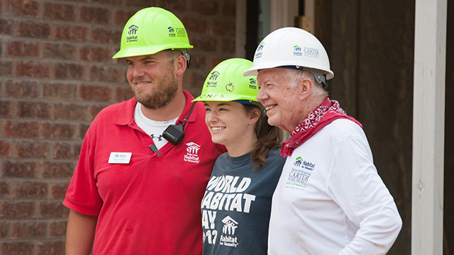 Sara and Taylor pose smiling with Jimmy Carter, all wearing hard hats 