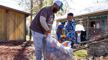 A man works with a young child to rake leaves into a bag at their neighborhood clean-up.