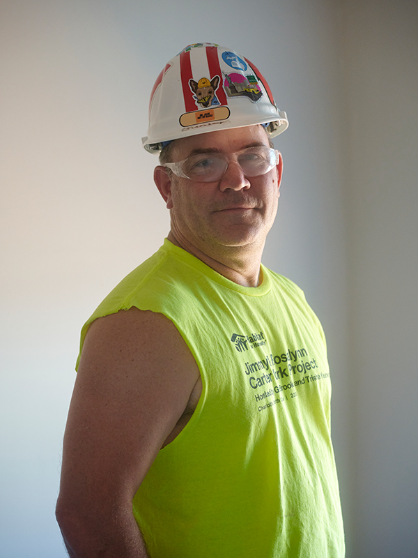 Chuck in a white hardhat with homemade stickers standing in a white room.