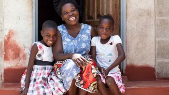 Photo: a women and two children from Zambia sitting on stairs in front of their house
