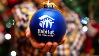 child's hand holding blue ornament with Habitat logo towards camera with bokeh background