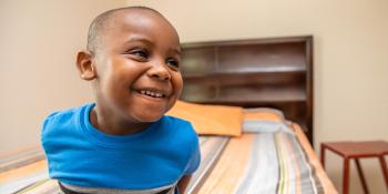 Boy smiling as he's sitting on his bed.