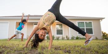 Two children do cartwheels in front of their family's Habitat house