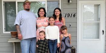 Sophia and Anthony pose smiling with their 4 children on the porch of their Habitat home.