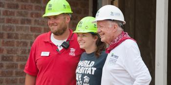 Sara and Taylor pose smiling with Jimmy Carter, all wearing hard hats 