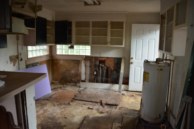 Dilapidated kitchen with rotting flooring and missing appliances.