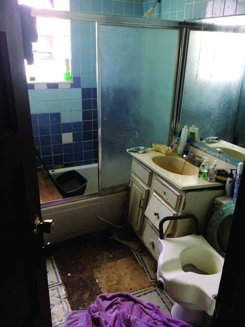 Bathroom with flooring, tile, and sink cabinet visibly falling apart.