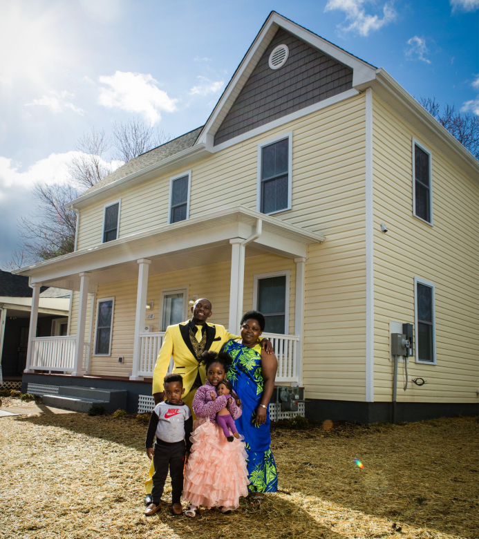 House with new roof, new siding, and fresh yellow paint with family of four in front.