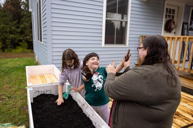 Habitat homeowner and her two daughters plant vegetable seeds in the front yard of their Habitat home.