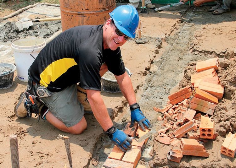 Neale Kemp kneels on the ground laying brick in the foundation of a Habitat house.