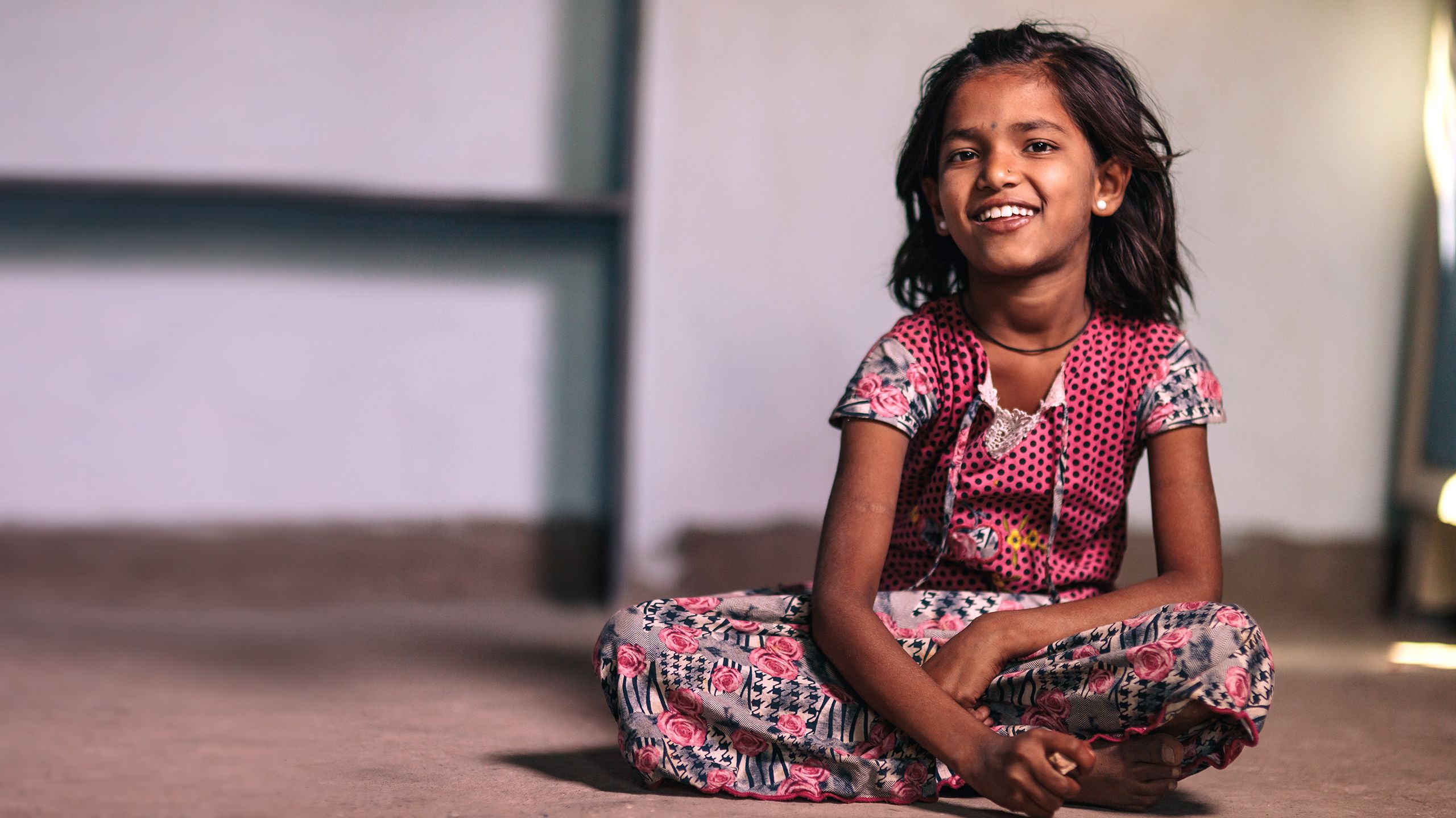 Aishwarya, a young girl, sits cross-legged on the new concrete floor of her home in Karnataka, India.