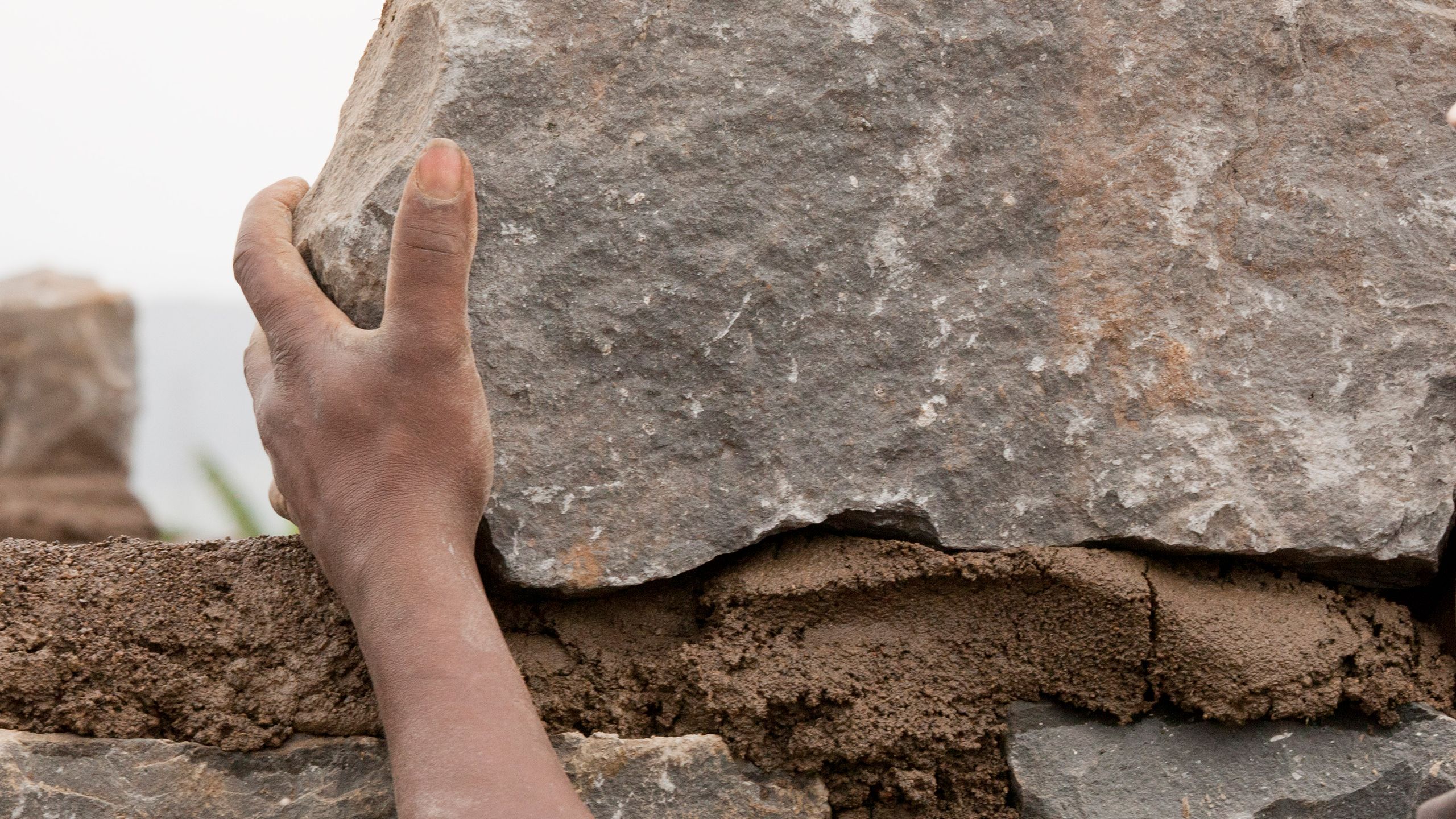 A large stone is set into mortar for a home's wall.