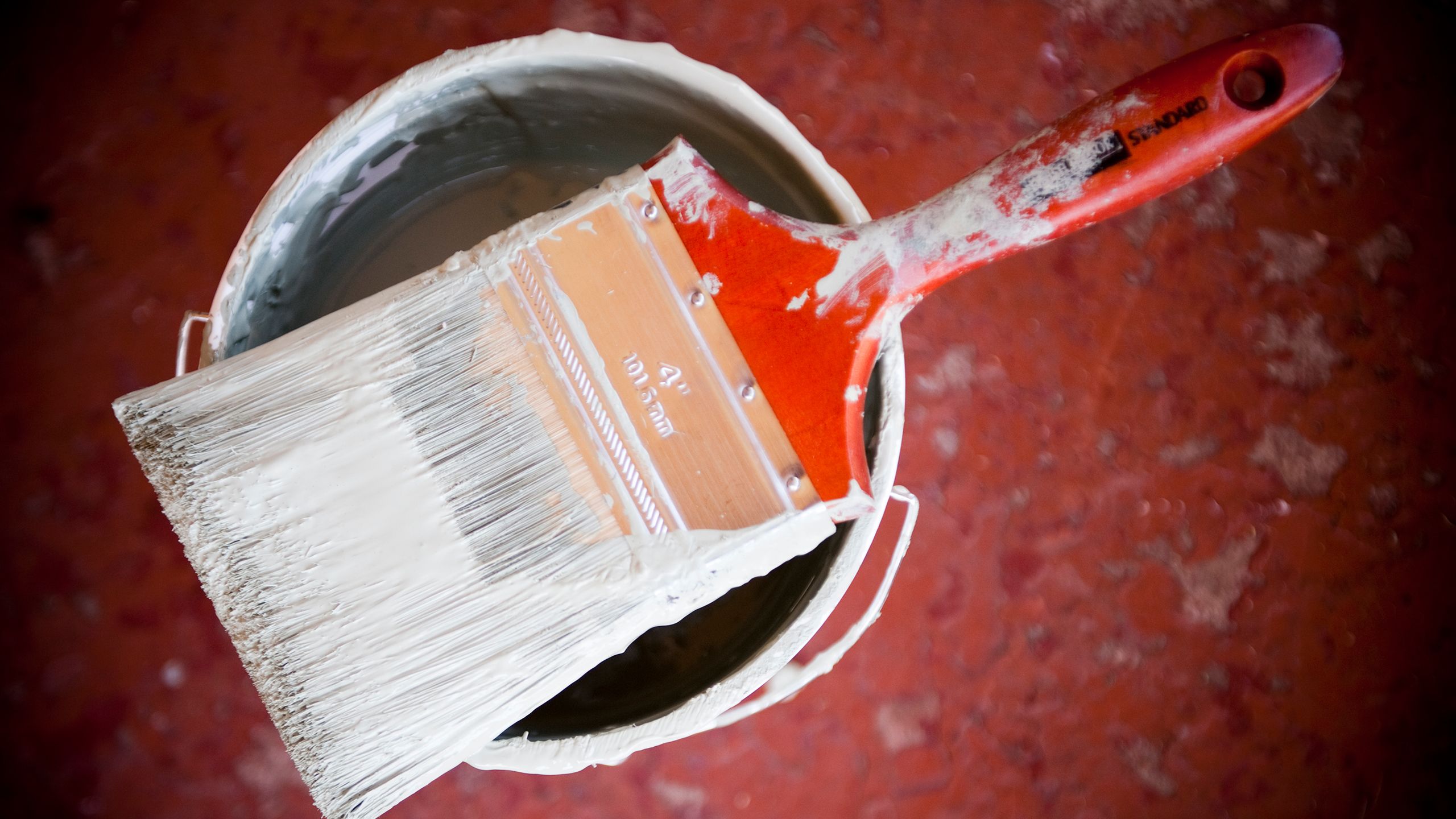direct down shot of a paintbrush on an open can of white paint, on top of a red background