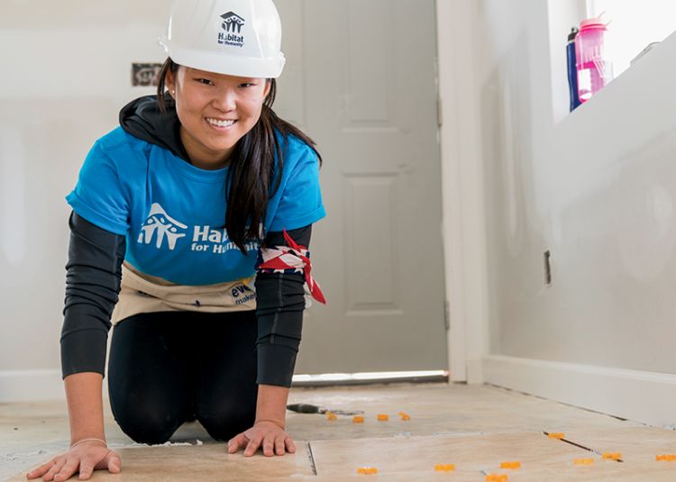 Michelle kneels to lay floor tile inside an unfinished Habitat house.