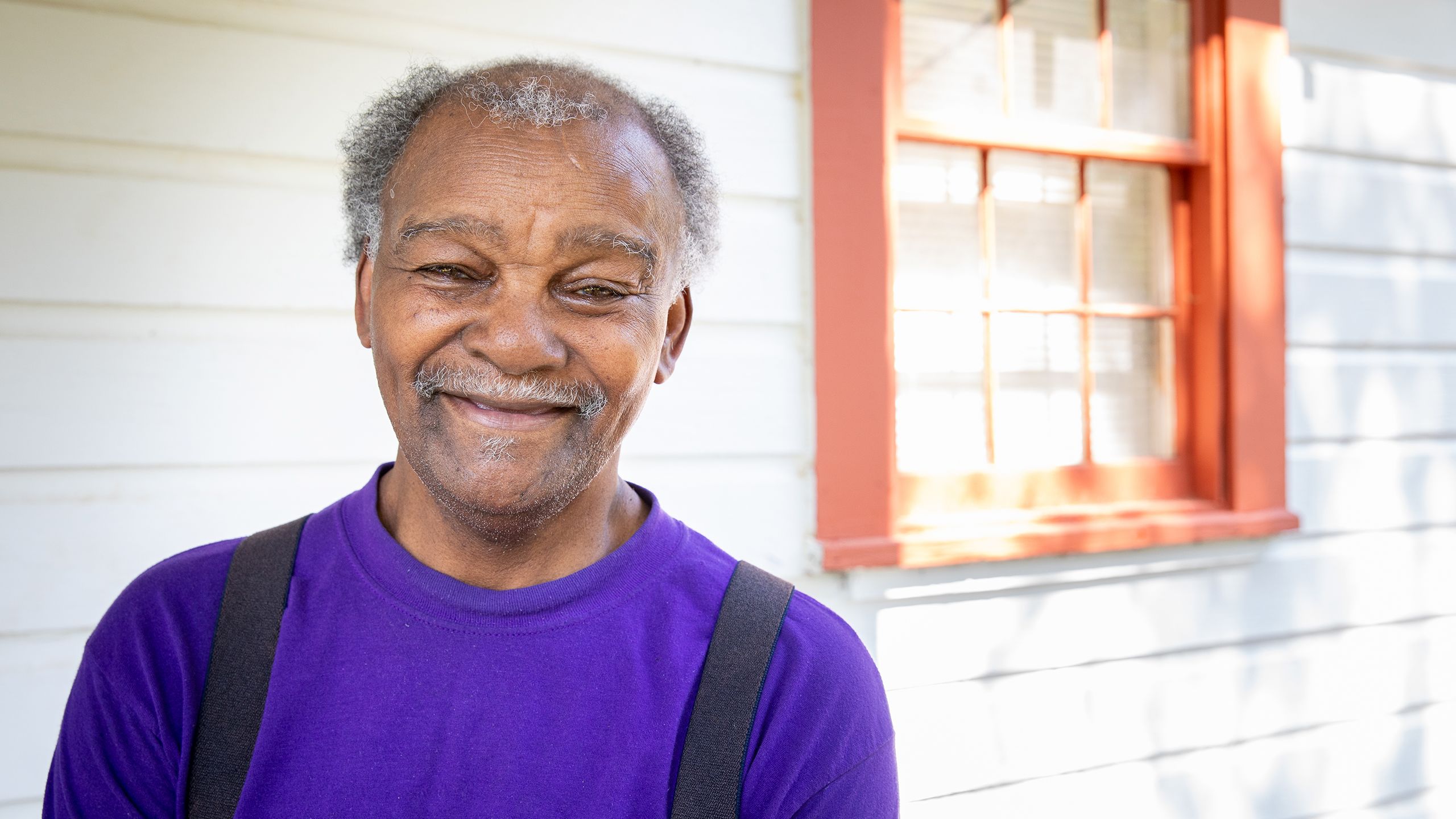 Walter (an older, balding black man wearing a purple shirt and suspenders) stands outside his home.