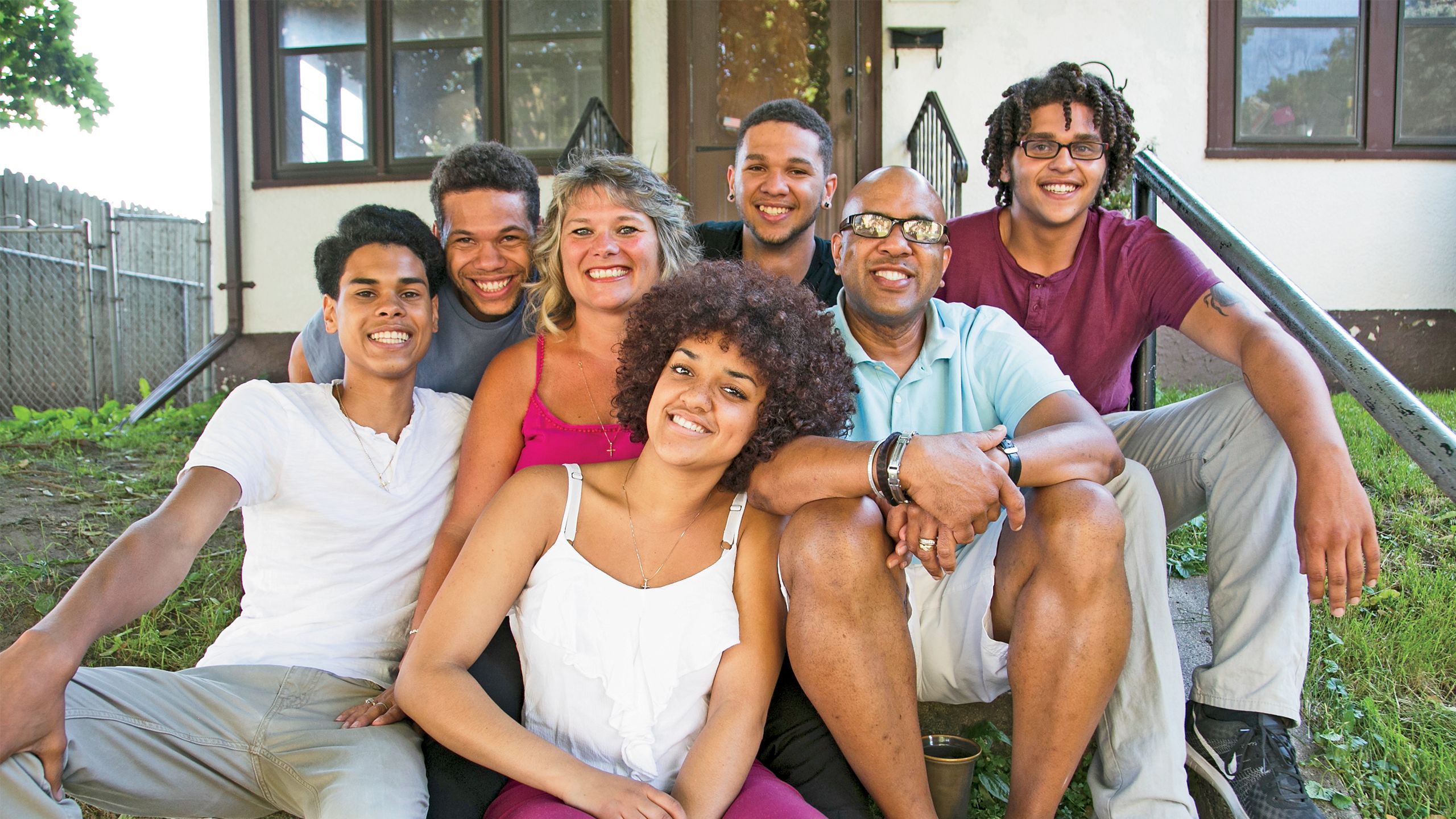 Juanita, her husband, and her kids (four young men and a young woman) pose, smiling, on the front steps of their Habitat home.