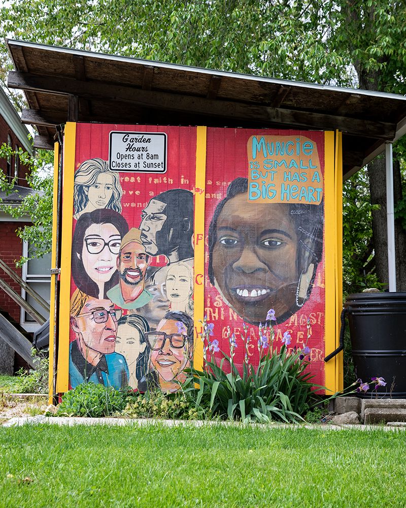 A mural on the side of a garden shed in a Muncie neighborhood, showing a grouping of diverse faces and the words "Muncie is small but has a big heart."