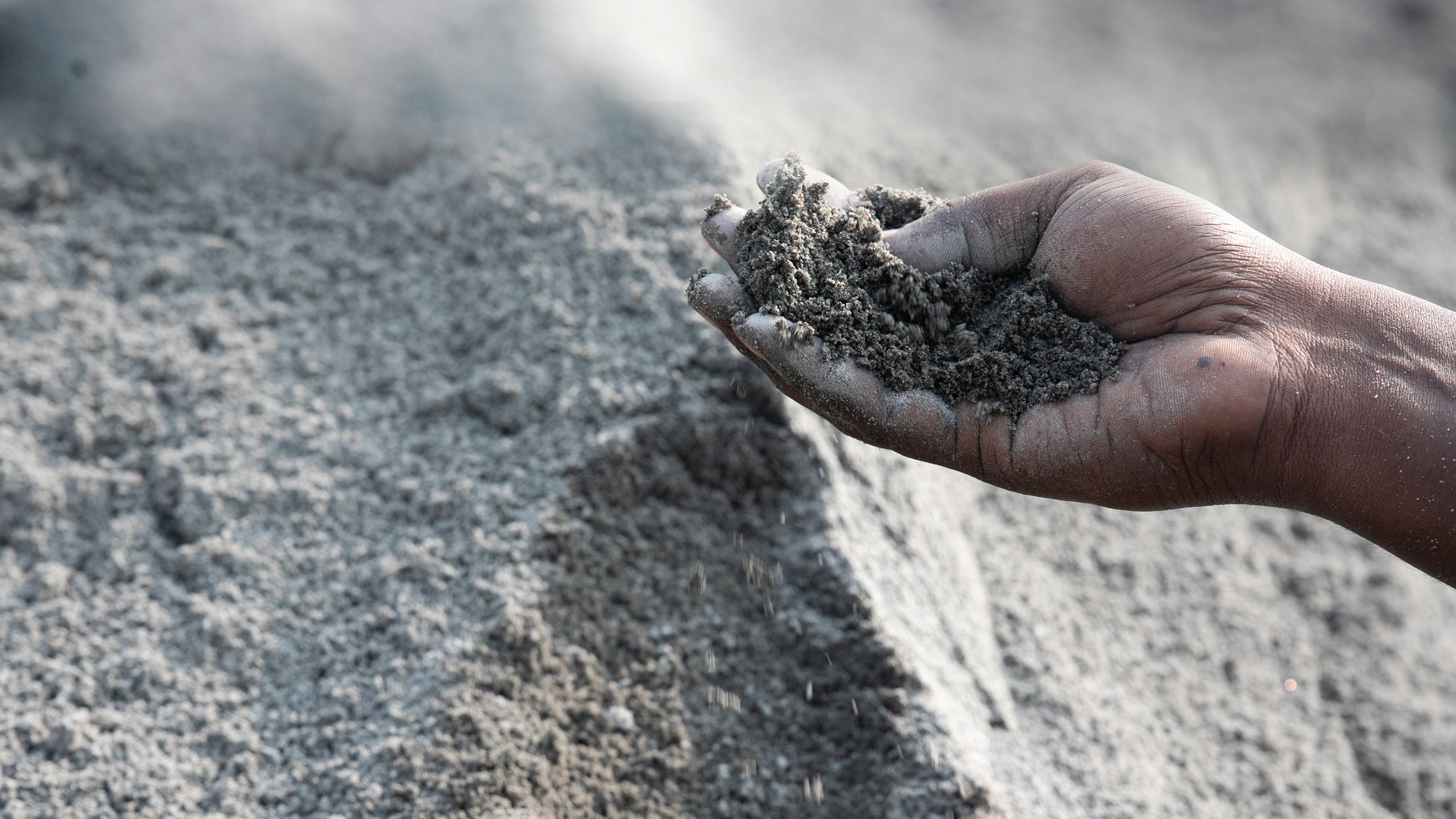 A worker holds out a handful of finished M-sand from a large pile.