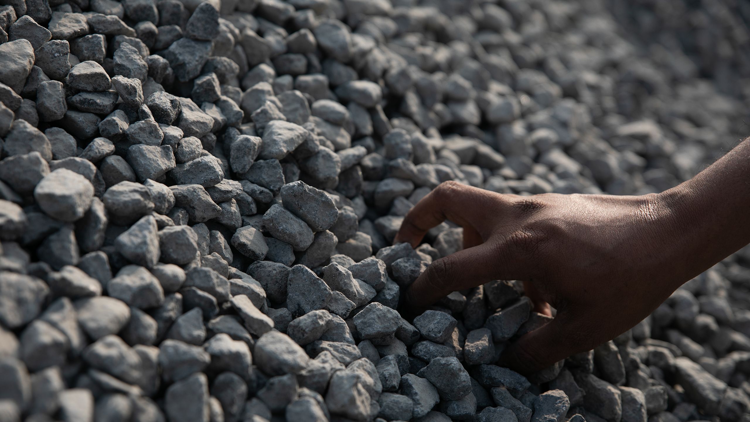 A worker grabs a handful of thumb-sized rocks from a large pile.