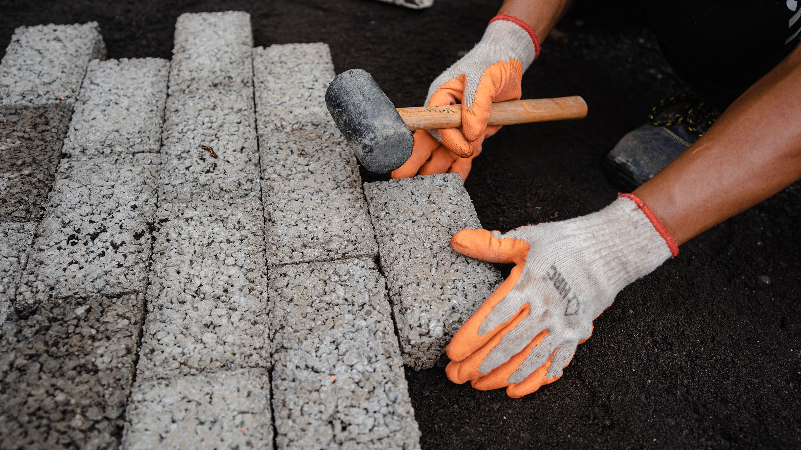 A mason lines up and lays concrete pavers on the ground.