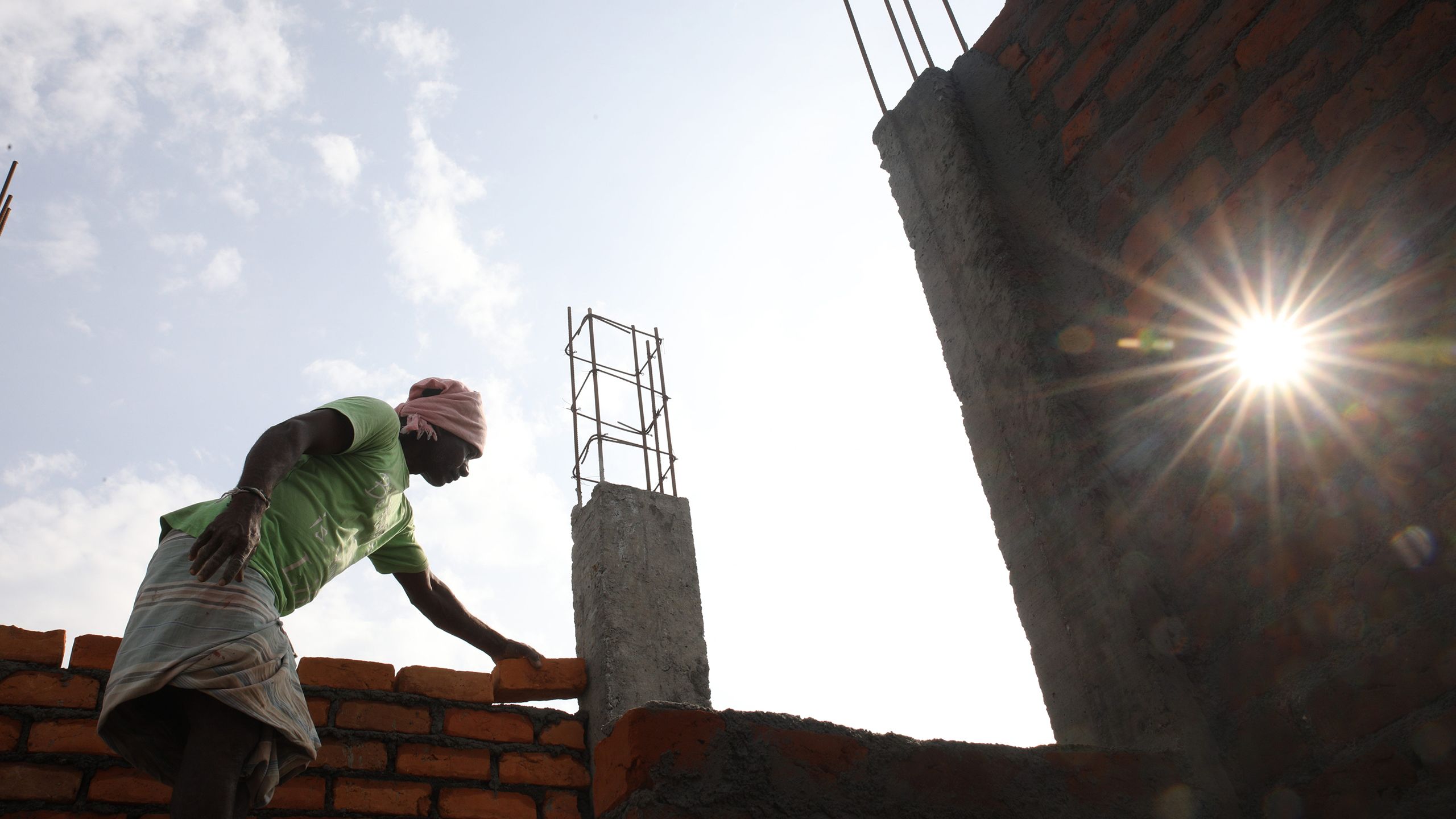 Hands in bright orange gloves stack concrete bricks into a wall.