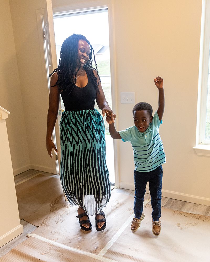 The woman jumps up with her son as he dances just inside the doorway.