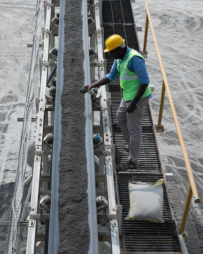 A worker stands next to a conveyer slide full of finished M-sand.