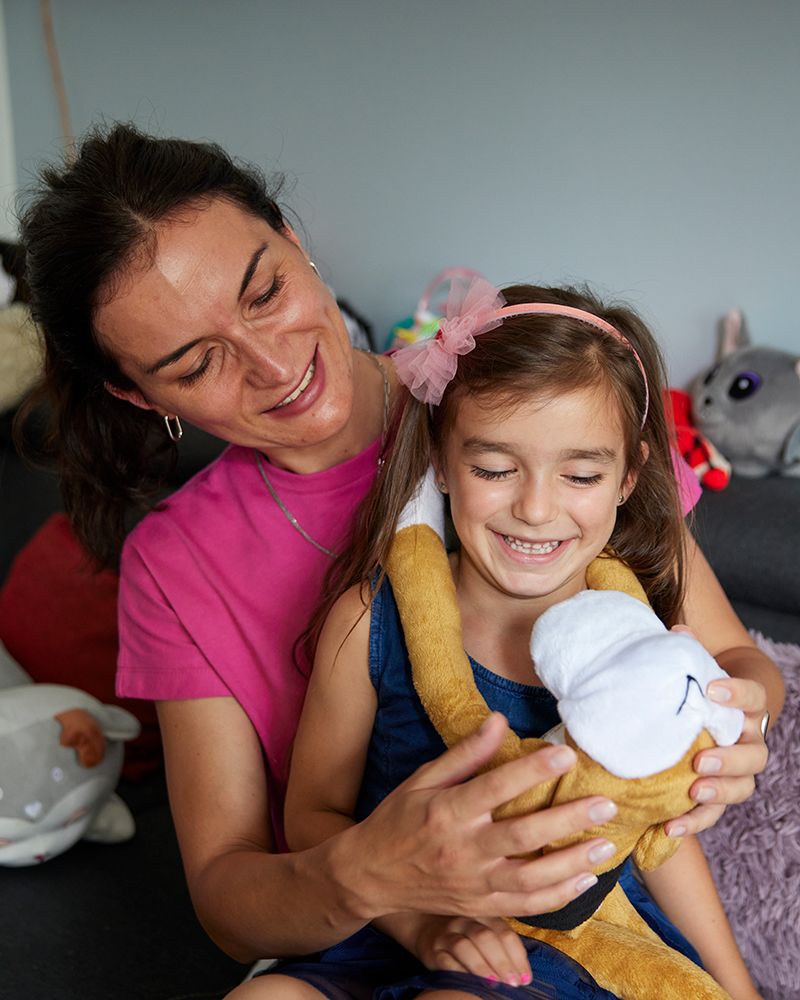 Iryna and her daughter Kira sit on the couch of their apartment in Poland, surrounded by Kira's stuffed animals.