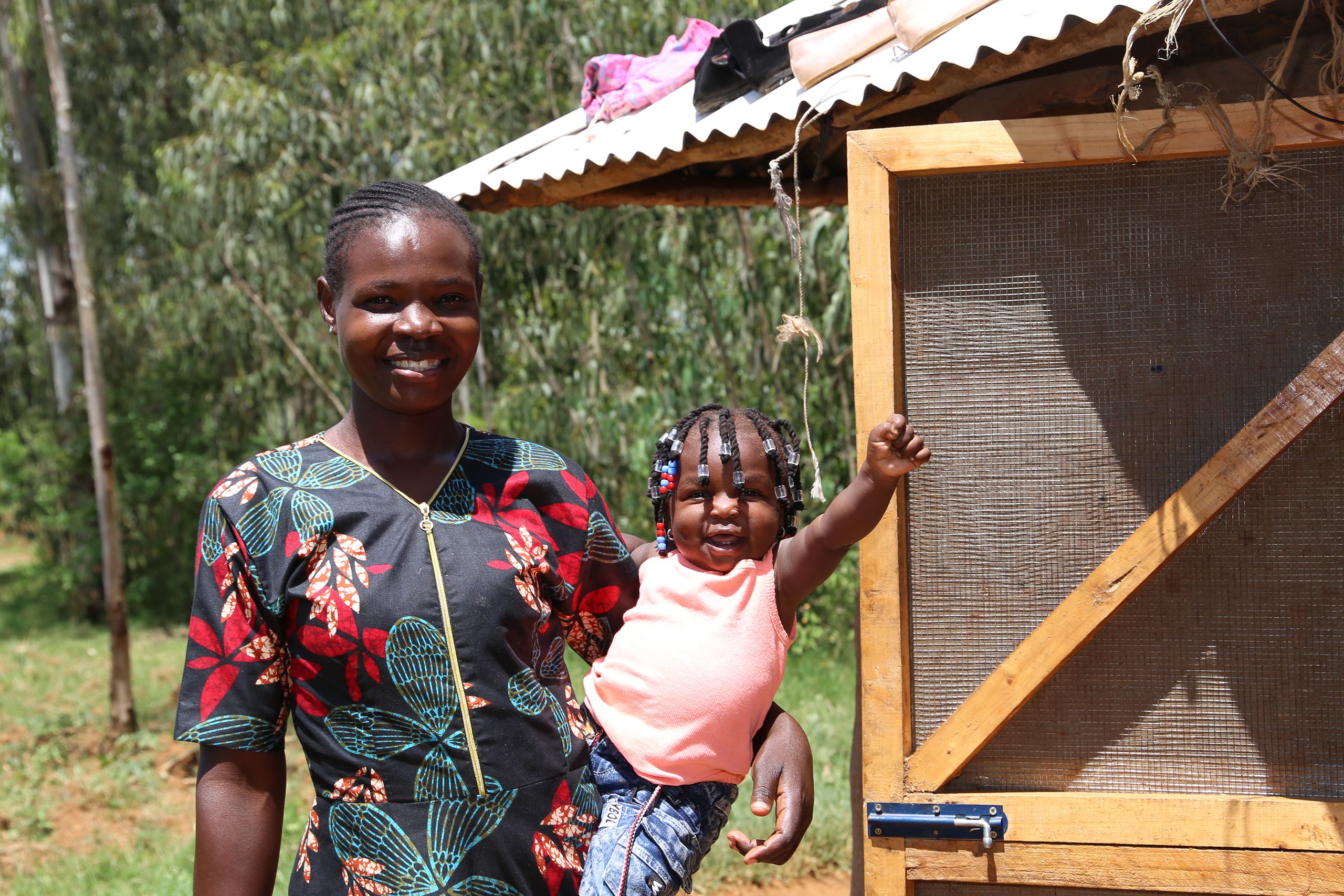 A mother and her toddler daughter smile as they stand just outside the screen door of their home.