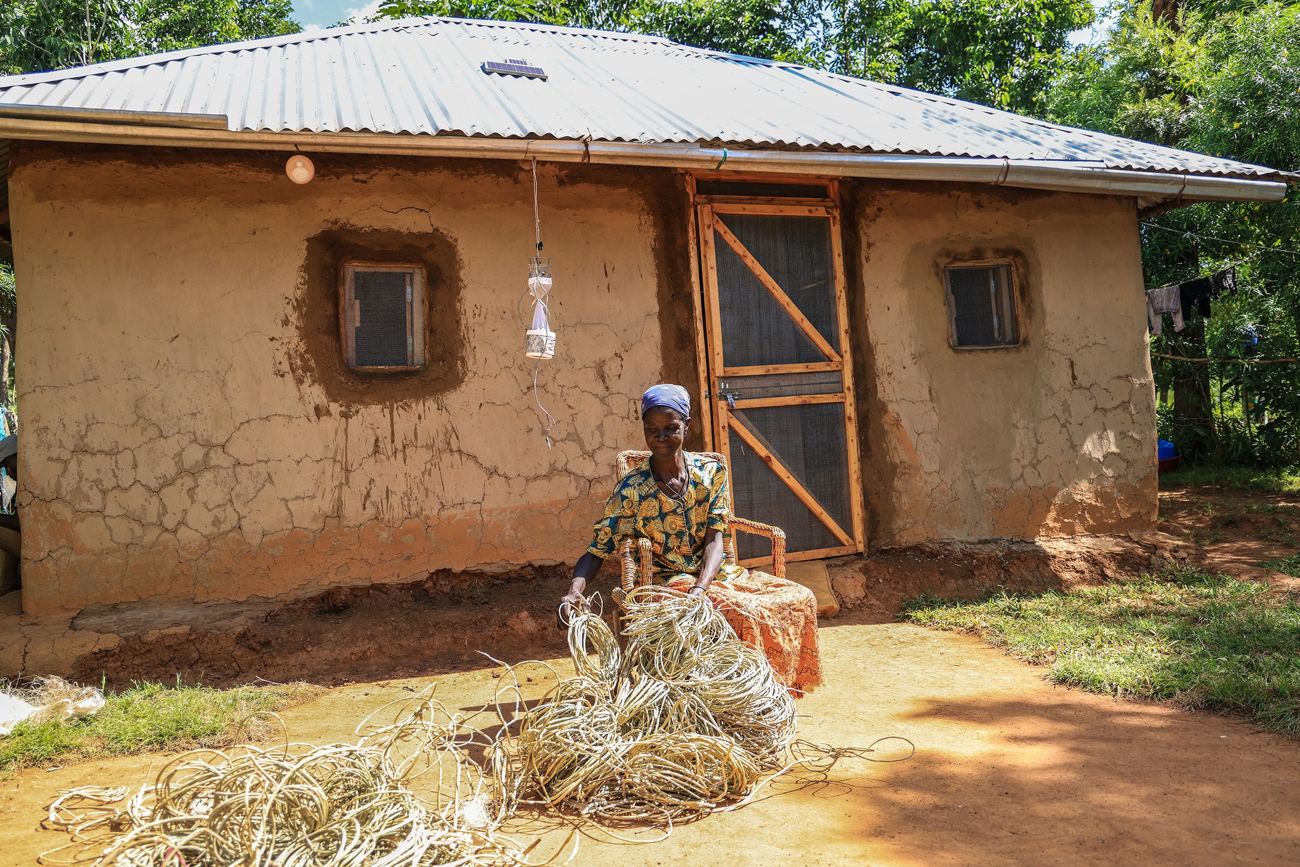 A woman sits weaving baskets in the front of her house with new screens