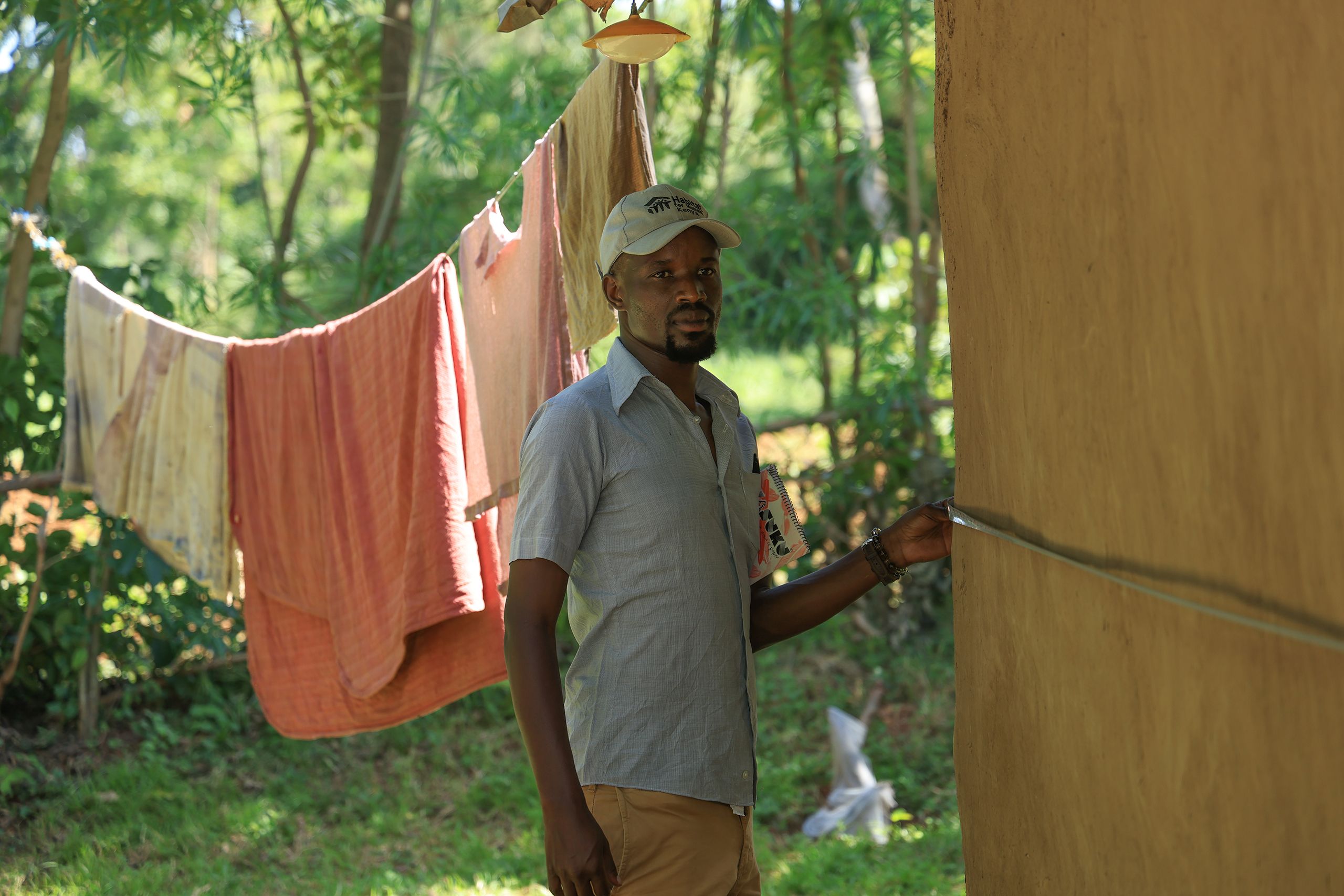 A Habitat Kenya staff member measures the exterior wall of a home.