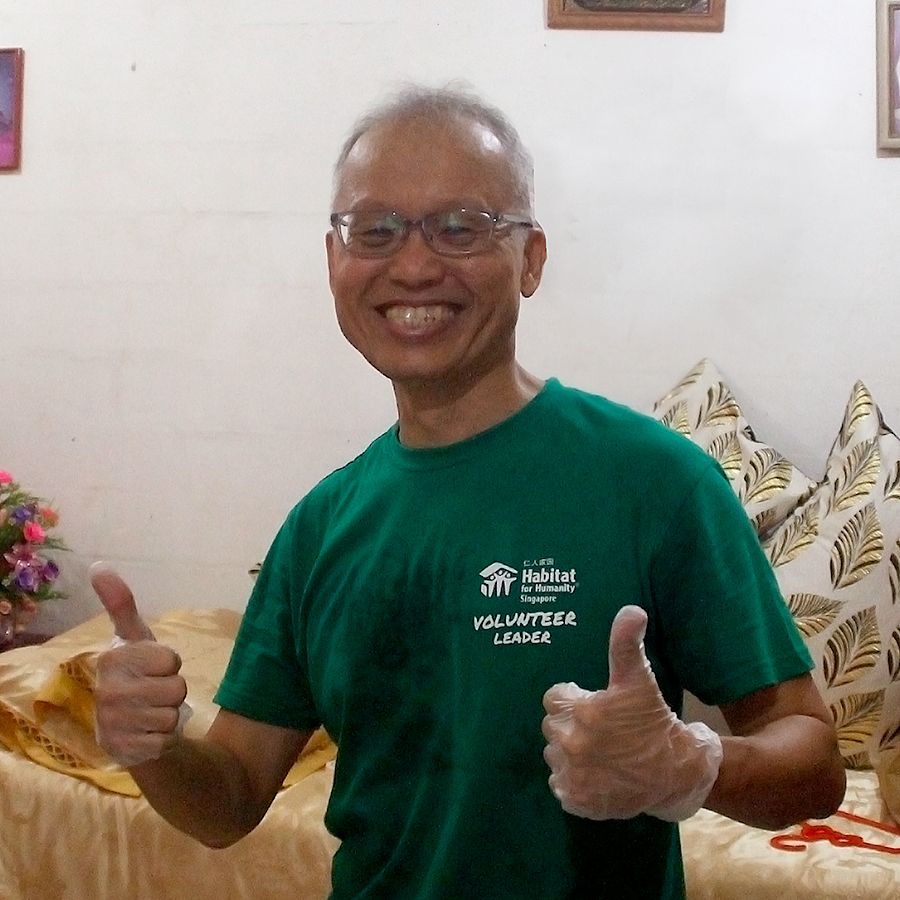 Wee Jin, a balding man in a green t-shirt with "Habitat Singapore Volunteer Leader" on the chest. He grins and gives two thumbs-up to the camera.