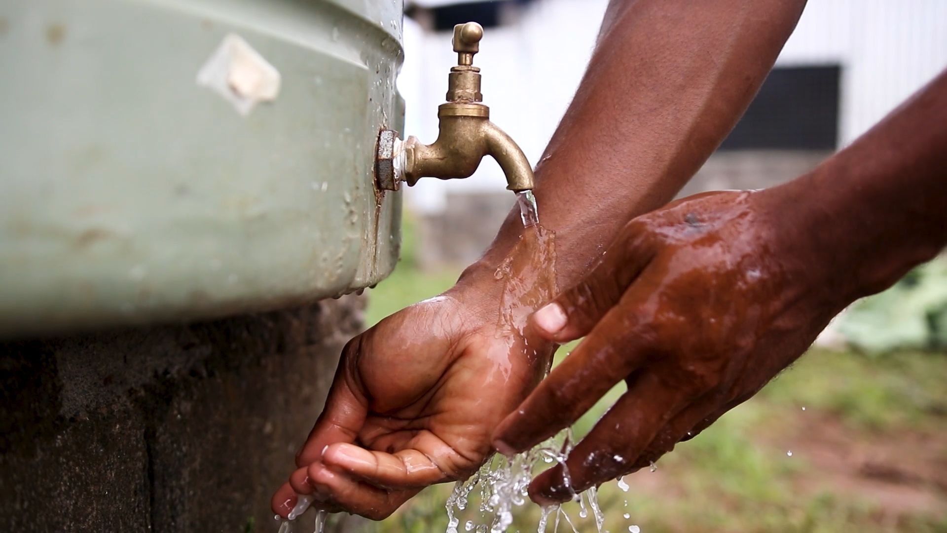 Closeup on a person washing their hands with water from a rain barrel.