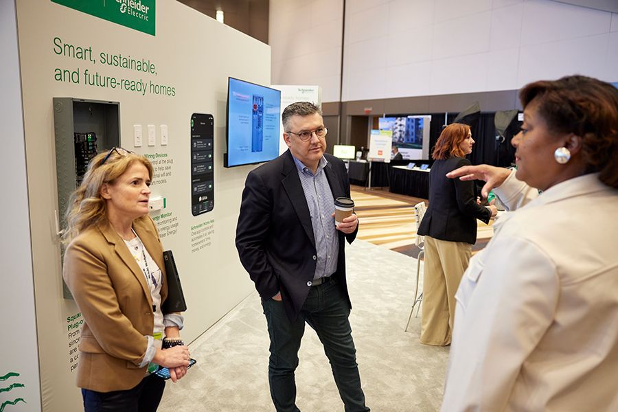 Two representatives from Schneider Electric are in conversation with a Habitat senior leader while standing in their booth at Habitat's Affiliate Conference. The booth shows examples of donated products like an electrical panel and wall switches.