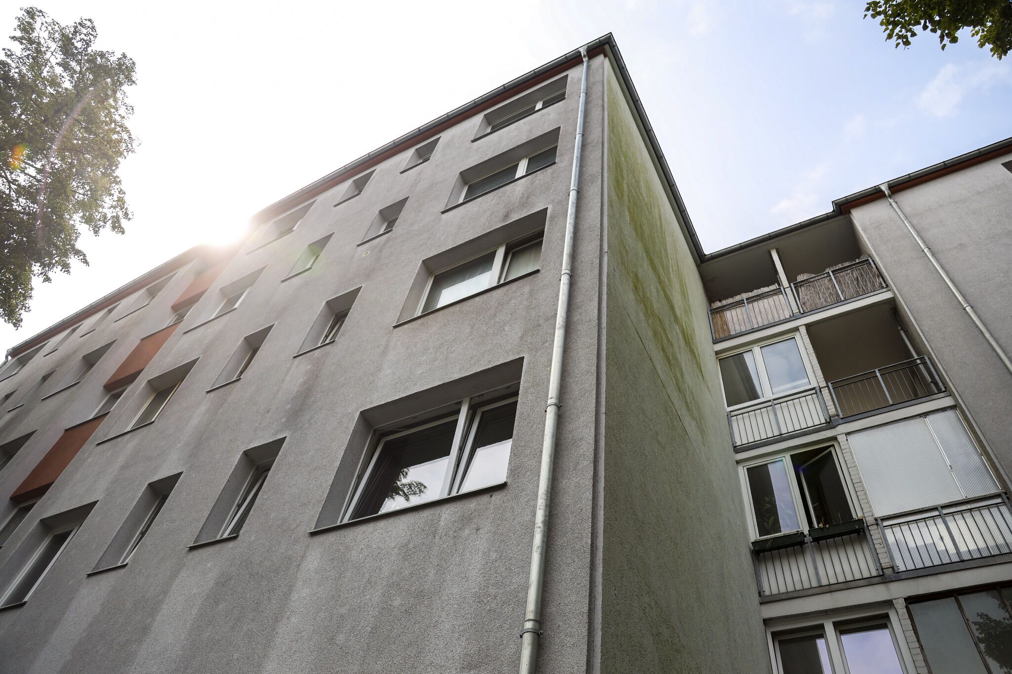 Upward view of a concrete apartment building. The sun shines from just behind the rooftop in a clear sky.