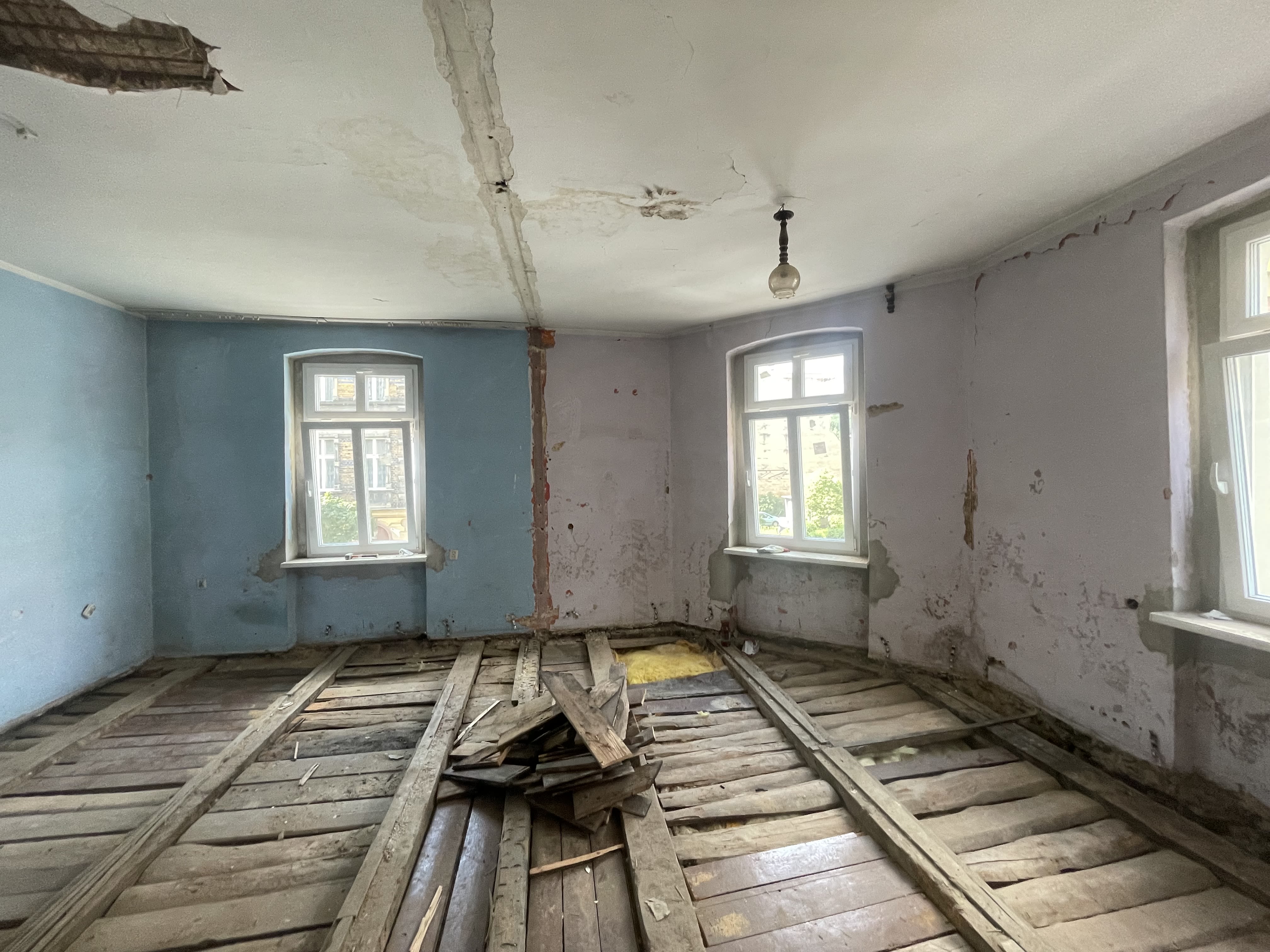 Before photo of an apartment that has broken floors and detcaying windows and walls.