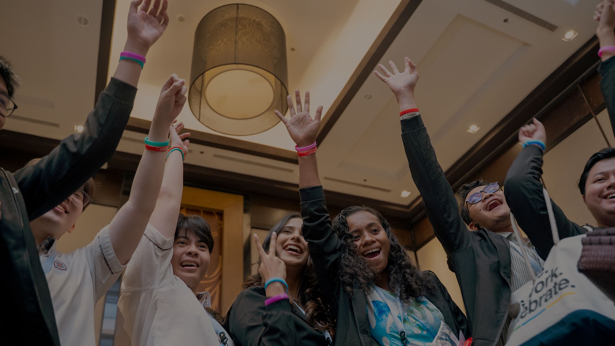 Attendees at the Youth Assembly enthusiastically raise their hands together in a circle..