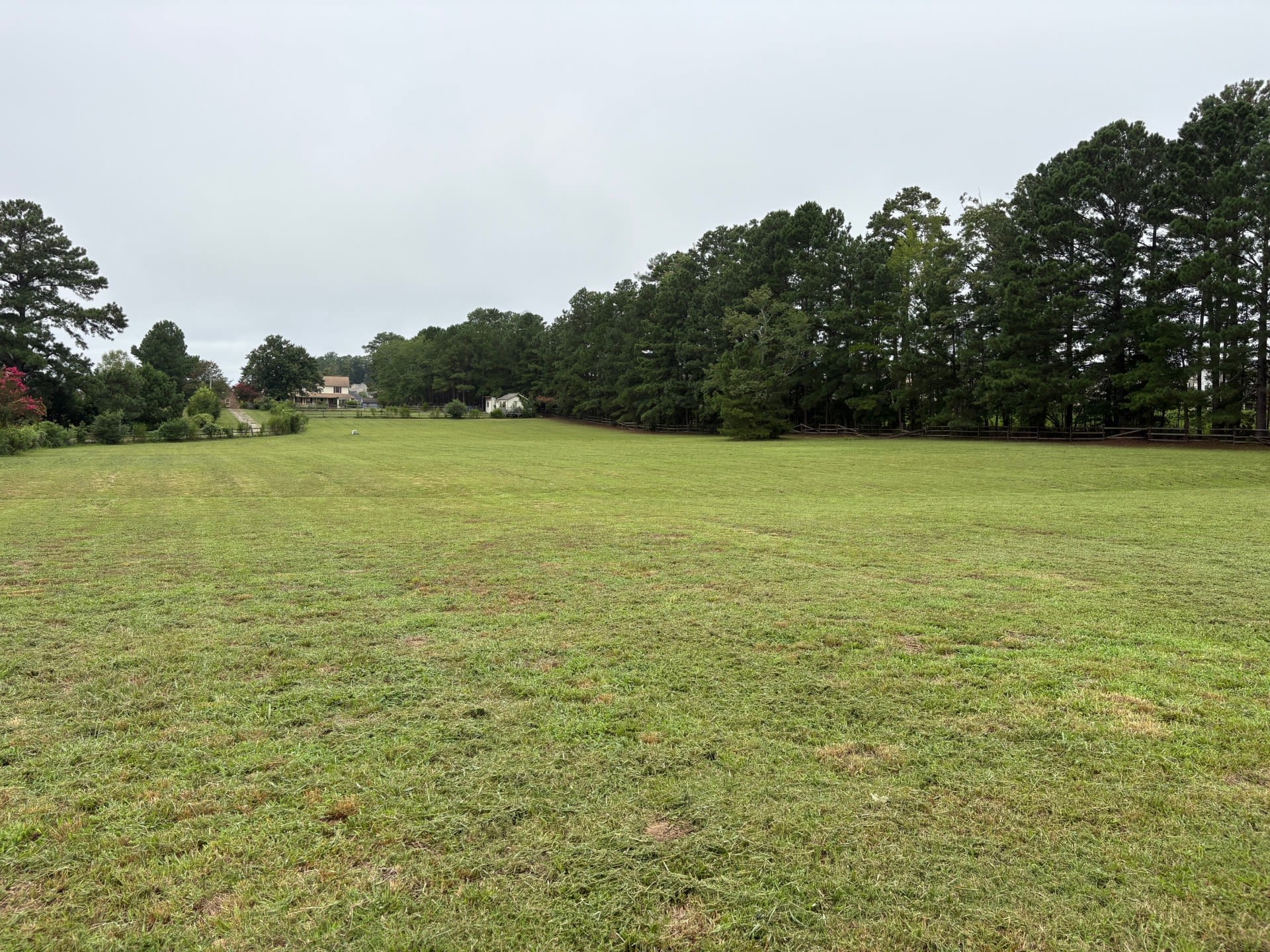 A plot of grass-covered land awaiting construction, lined with trees and with other houses visible in the distance.
