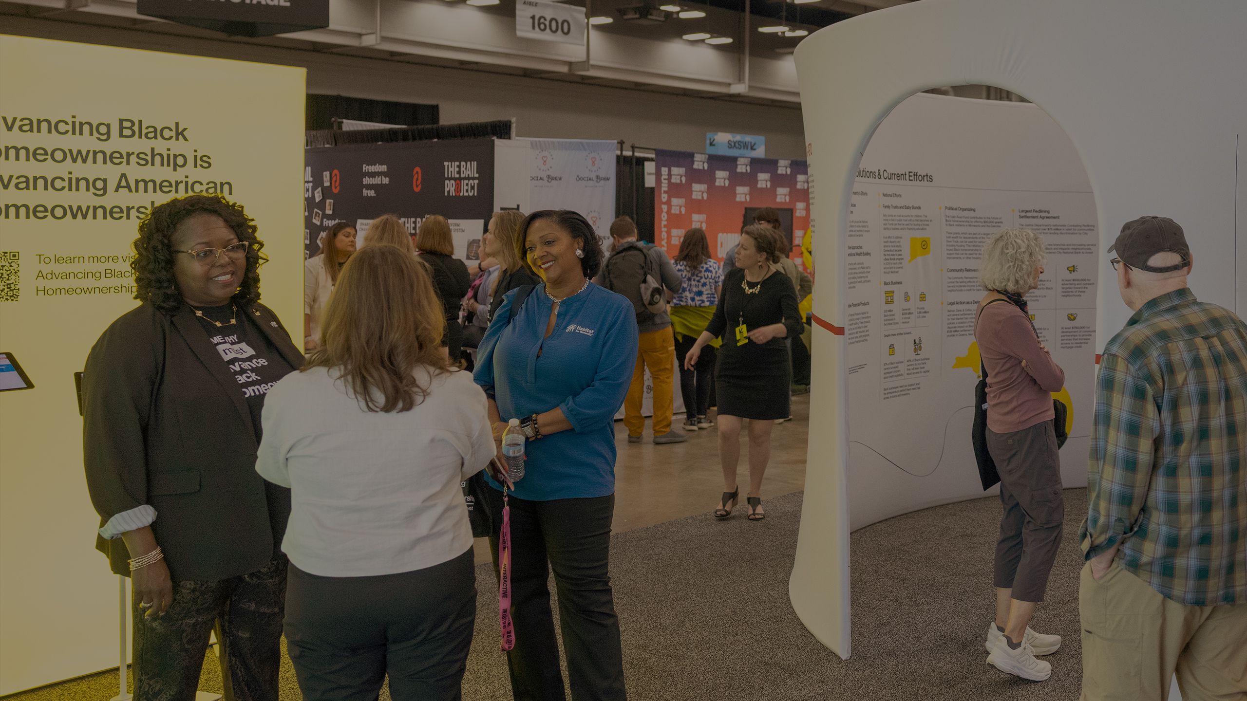 Event attendees step through the exhibit, a timeline of significant events in the history of racial equity and housing in the US. Nearby, two Habitat leaders chats with an attendee.