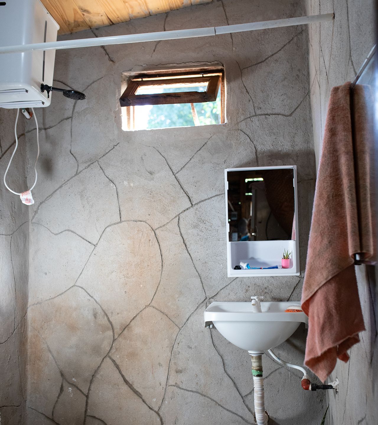 Interior view of the bathroom Maria Alejandra installed, showing a small sink, showerhead with hot water tank and medicine cabinet with a tiny potted plant perched on the shelf..