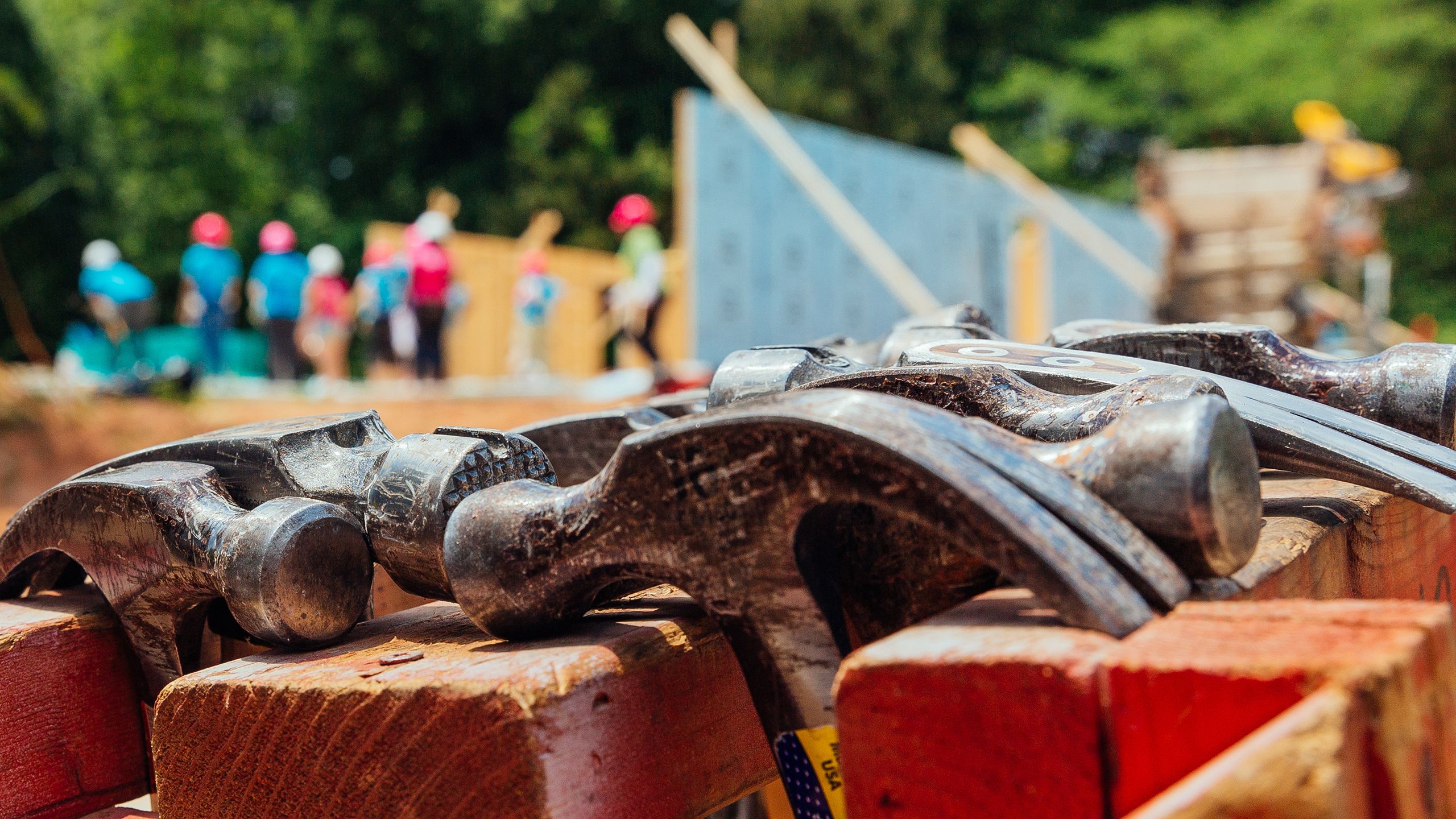Closeup on a rack of hammers in the foreground, as Habitat volunteers work on a build site in the background.
