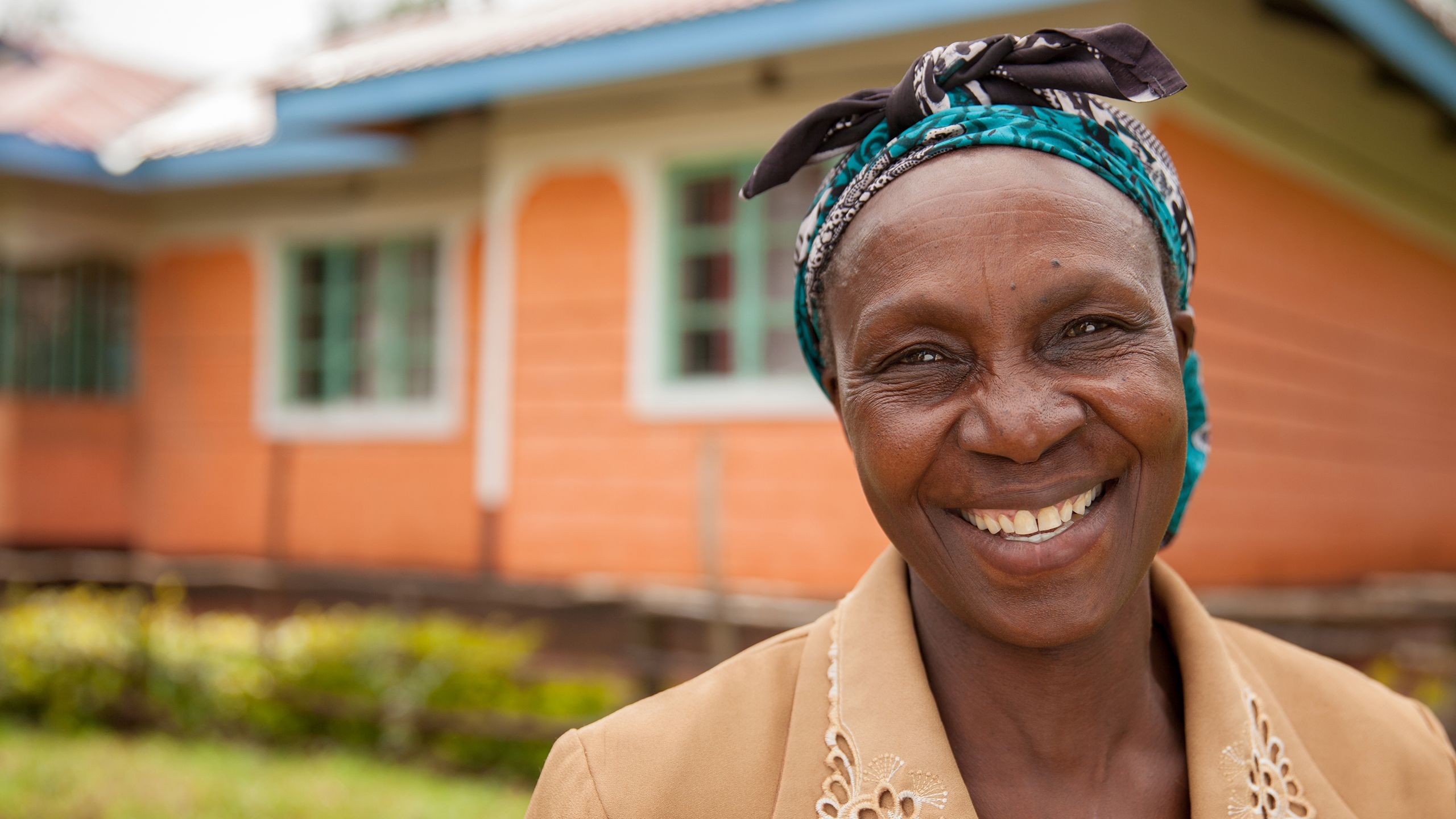 A smiling woman stands proudly in front of her Habitat house in Kenya.