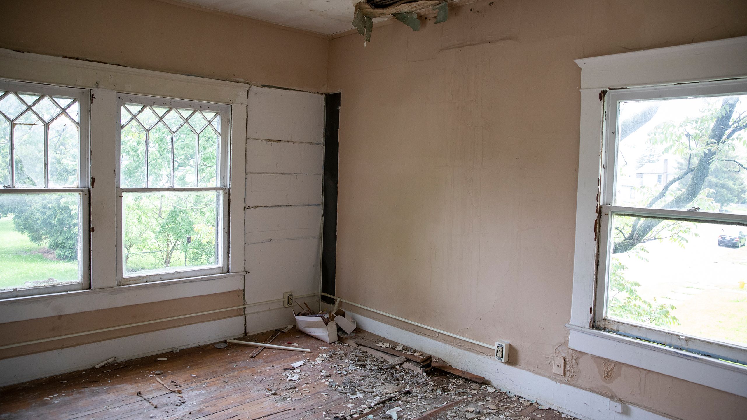 The interior of an aging house with peeling paint, crumbling drywall, debris covering the floor, and the ceiling caving in.