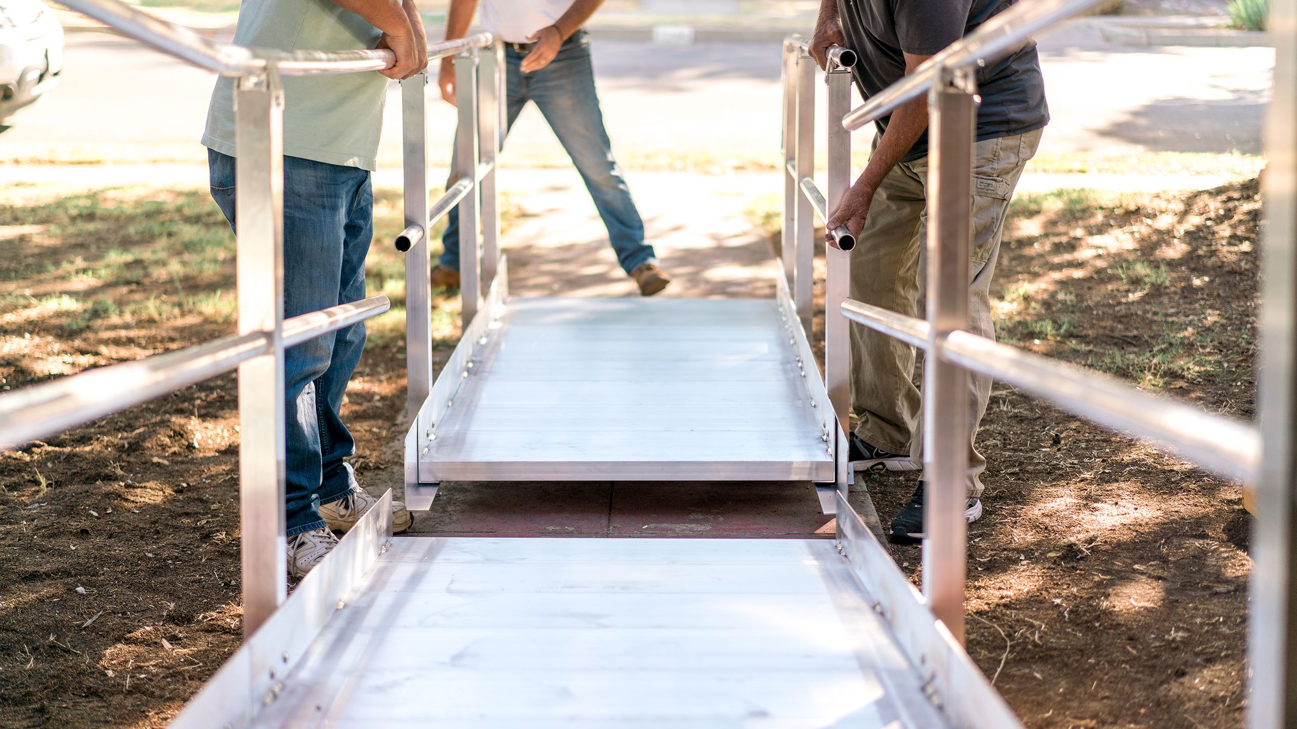A group of people installs a metal wheelchair ramp in front of a house.