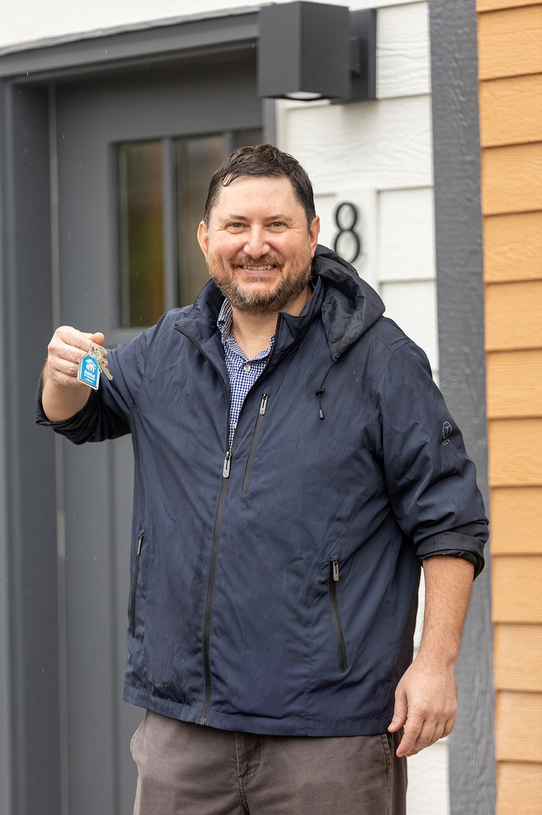 A man with a graying beard grins as he holds up the key to his Habitat home.