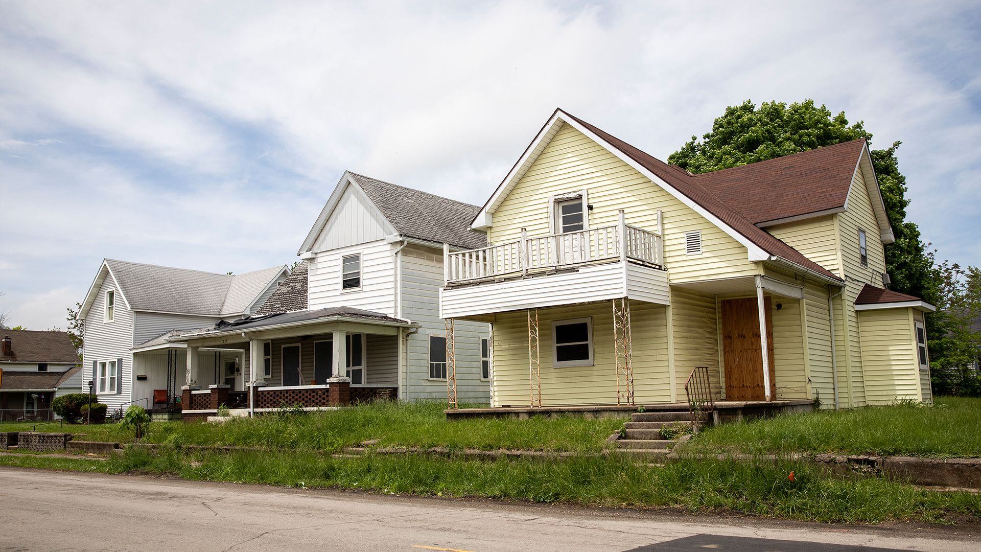 A row of visibly deteriorating homes with rusting metalwork, crumbling siding and brickwork and weedy lawns.