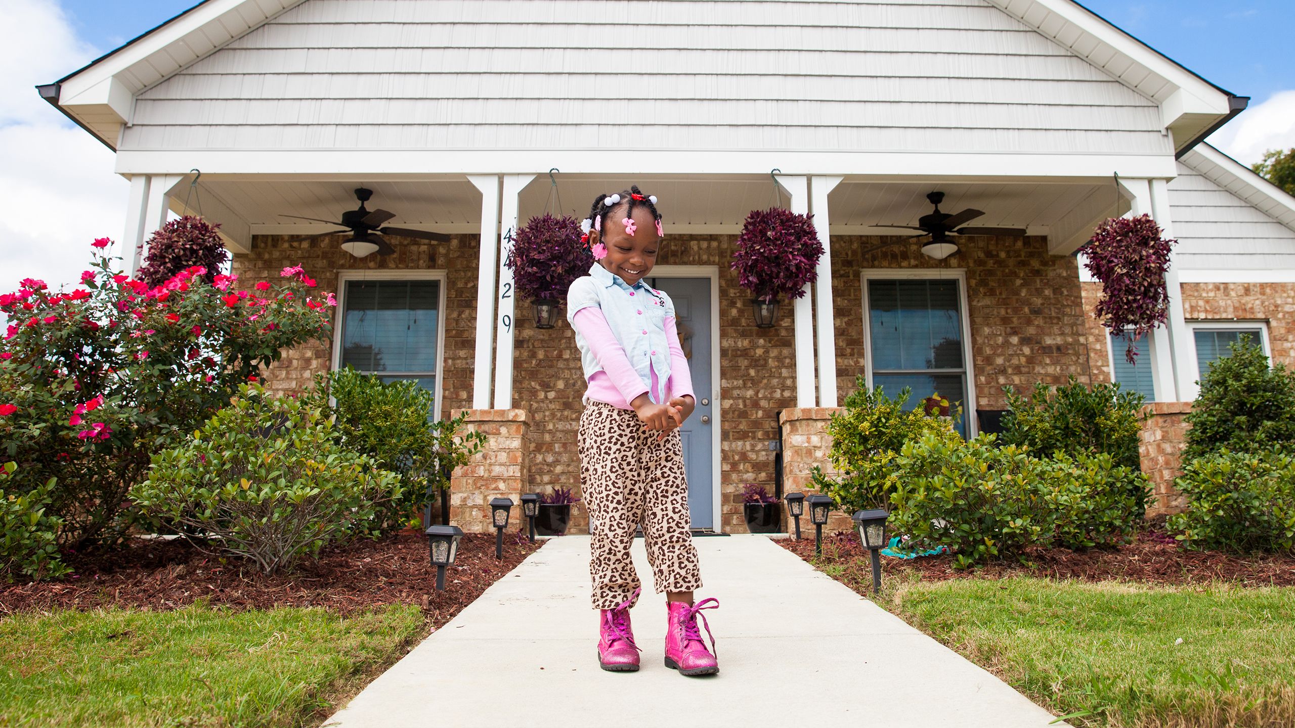 A young girl stands in front of the Habitat house her mother worked to build.