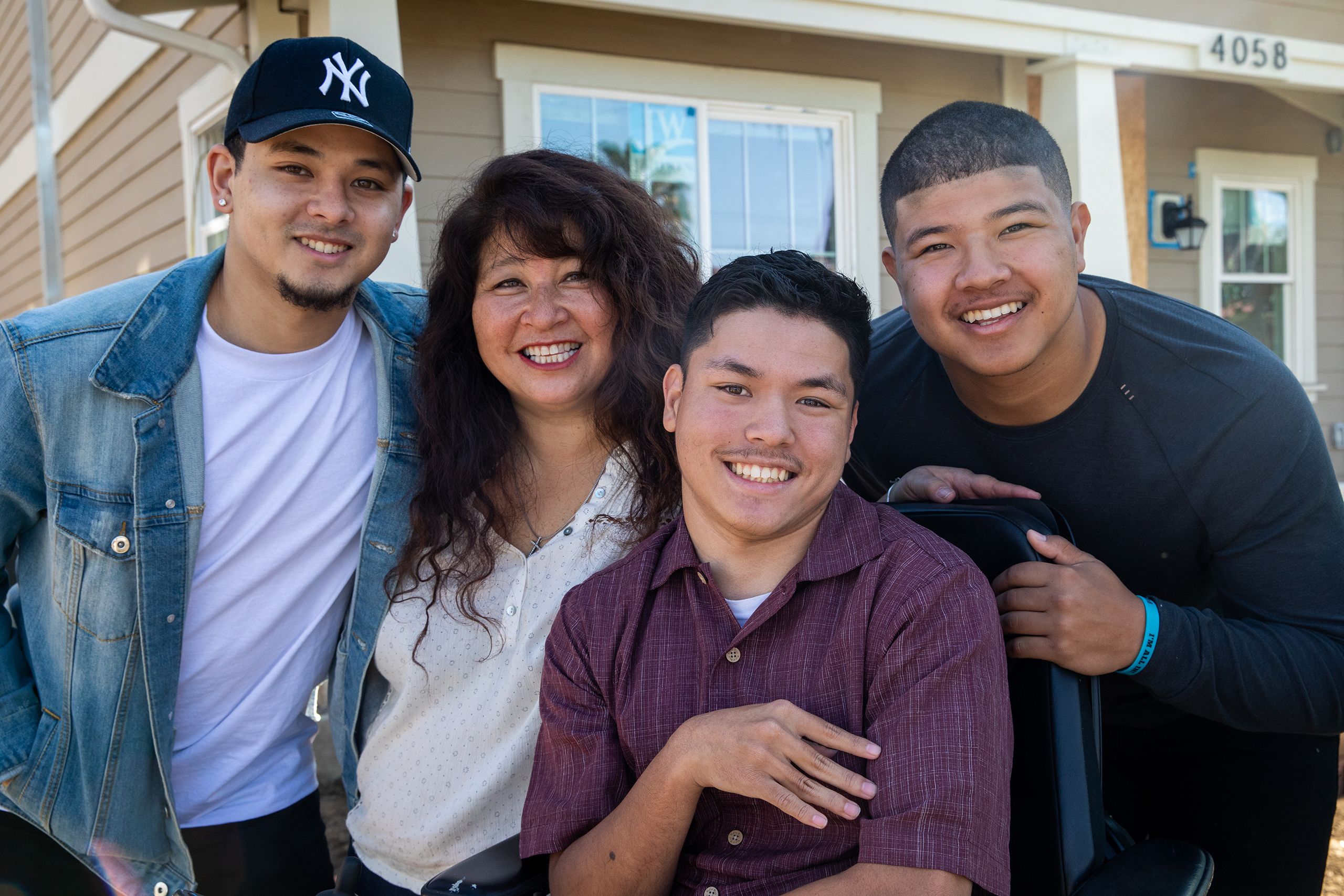 A mother and her three teenage sons, one in a wheelchair, stand in front of their newly built home.