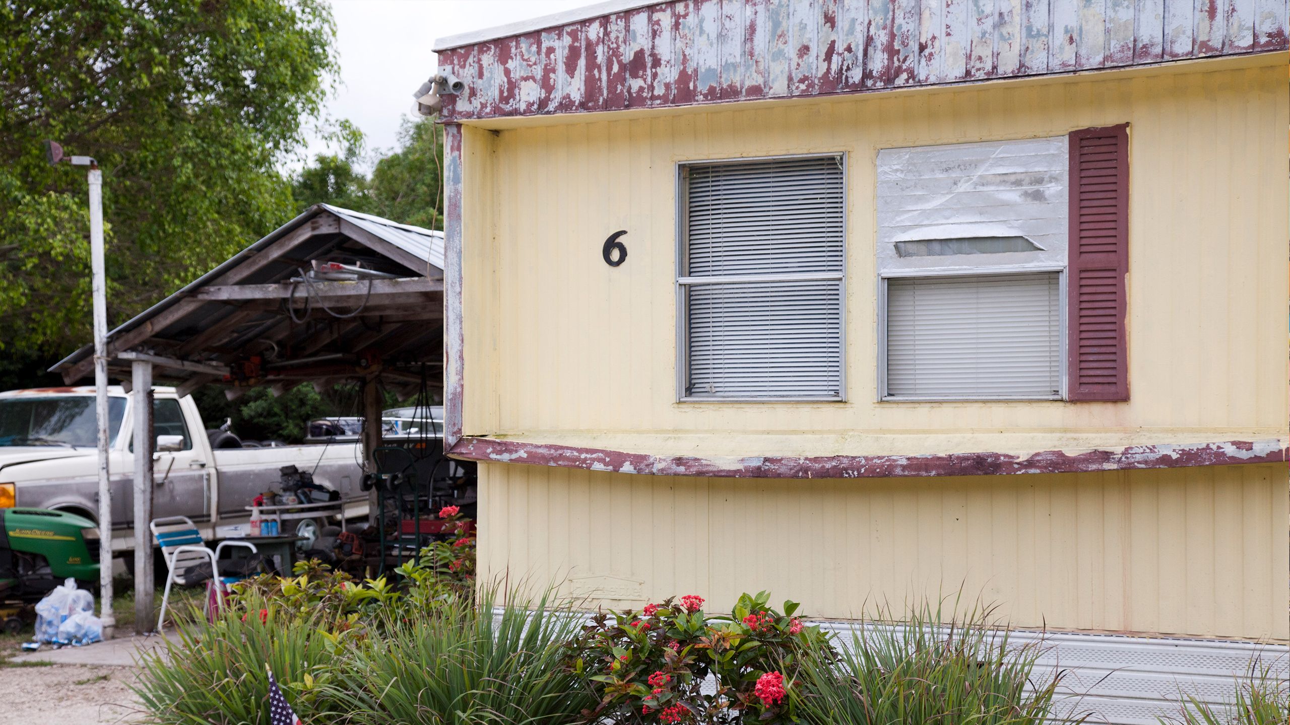 Exterior of a mobile home with degrading siding and a broken window.