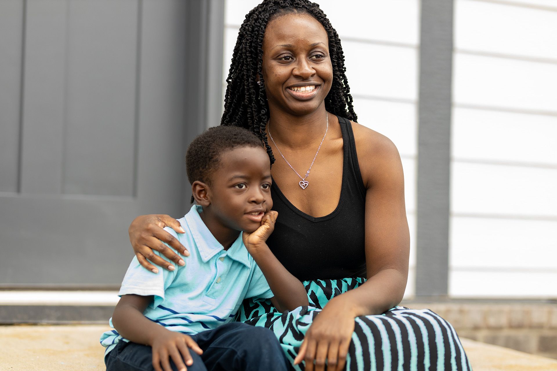 A mother and her young son sit on the stoop of their newly completed Habitat home.
